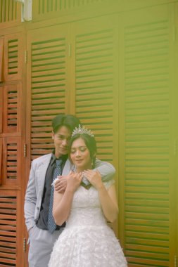 Zarif pozlar veren bir çift kadın ve erkek eli gülüyor. Kadının vücudunun arkasından sarılıyorlar. Parktaki bir fotoğraf çekiminde güzel bir elbise giyip gözlerini kapatıyorlar.