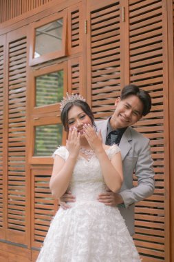 Zarif pozlar veren bir çift kadın ve erkek, parkta çekilen bir fotoğraf çekiminde güzel elbiseler giyip kadın elleri ile gülüyorlar.