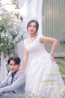 Bir çift erkek ve kadın zarif bir poz veriyor. Kadın ayakta duruyor ve erkek romantik ve samimi oturuyor. Parkta güzel elbiseler giyiyor.