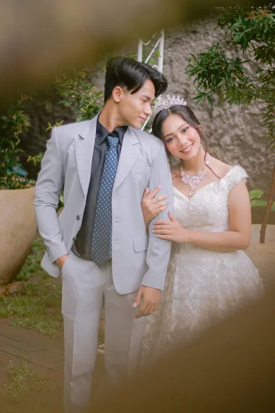 Bir çift zarif kadın ve erkek, bir sırada durup kameraya üstten bakan kadına bakıyorlar. Parktaki fotoğraf çekiminde güzel elbiseler giyiyorlar. Ulusal Gelin Açık havada düğün çifti