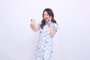 Çin malı mavi elbiseli genç Asyalı kadın Cheongsam 'ı telefonda kameraya bakarken hayal kırıklığına uğrattı.