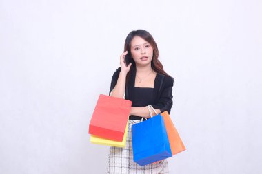 Güzel Asyalı kadın müşteri 20 'li yaşlarda resmi ofis şok oldu telefonda kollarını kavuşturup alışveriş poşeti taşırken beyaz arka plan izole edildi.