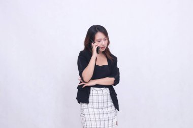 20 'li yaşlarda güzel bir Asyalı ofis kadınının cazibesi, kollarını kavuşturmuş, beyaz bir arka planda izole bir şekilde cep telefonuyla sohbet eden bir kadın.