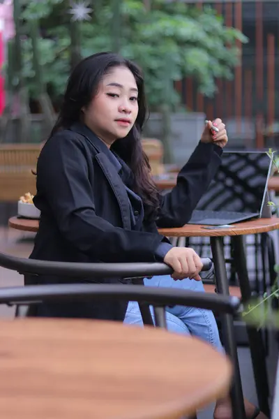 portrait of a beautiful, elegant Asian woman meeting online with her friend in a zoom meeting holding a pen in a cafe