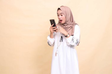 Başörtüsü takan genç bir Asyalı Müslüman kadın elinde dua boncuklarıyla akıllı telefon cihazıyla sohbet ederken şok oluyor. Reklam, yaşam tarzı, afişler ve Ramazan için
