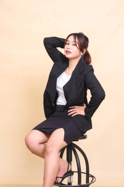 Endonezya 'nın genç ve güzel yönetici kadını sandalyede oturuyor ve elinde bel ve sırt kıllarıyla kameraya poz veriyor, ticari, boş ve iş yeri için sarı arka planda 3' e 4 vücut portresi