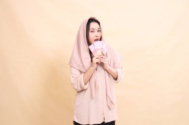 Asyalı kadın kameraya şaşkınlığını iki eliyle çenesine rupiah banknotları tutarak ifade ediyor. Finans, reklam ve moda için çok güzel.