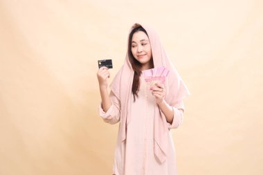 Asyalı bir kadın, elinde banka kartı ve rupiah parası tutarken gülümsedi. Finans, reklam ve moda için çok güzel.