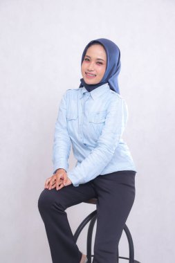 Endonezya 'lı genç bir ofis kadını mavi gömlekli bir tesettüre oturmuş, elleri kalçasında neşeli bir şekilde gülümsüyor. Güzel Müslüman kadınlar iş, finans ve moda içeriğini kullanır