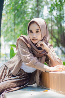 Güzel, zarif bir Asyalı kadın kameraya bakar seramiğe yaslanır ve kampüs parkında bir sandalyeye oturur. İnsan ilgi alanı ve yaşam tarzı konsepti için öğrenci