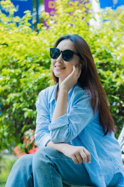 Endonezyalı, gözlüklü, açık hava bahçesinde oturan neşeli gülümsemeli olgun bir kadının portresi. Eğitim, teknoloji ve reklamcılık konuları için bayan öğrenciler