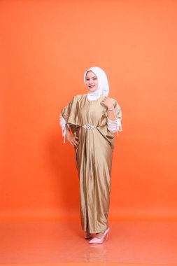 Endonezyalı genç, gülümseyen, kaftan başörtüsü takan, bel ve omuzlarıyla turuncu arka plan izole edilmiş bir kadın. İslam dini, moda ve ticari konsepti