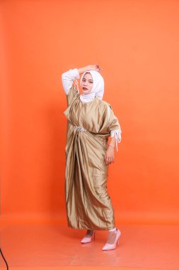 Kaftan başörtüsü takan, başı üstünde duran ve izole edilmiş turuncu arka planın yanında duran zarif Endonezyalı Müslüman bir kadın vücudu. İslam dini, moda ve reklamcılık kavramı