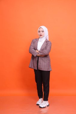 Turuncu stüdyo arka planında izole edilmiş tesettürlü şık beyaz ofis kıyafeti giyen güzel Müslüman kadın modelin tam boy portresi. Moda, güzellik, şirket, yaşam tarzı kavramı