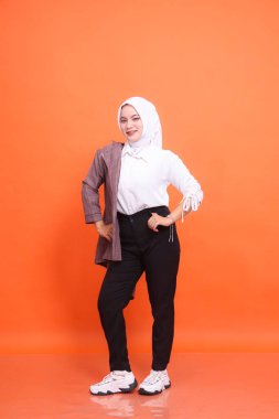 Asyalı güzel bir kızın, kemer cebinde, beyaz yarı ofis kıyafeti giymiş güzel bir gülümseme portresi portakal rengi bir arka plan. Moda kavramı, güzellik, arkadaşlık