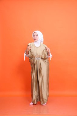 Kaftan tesettürlü, kaftan tişörtlü, turuncu arka planlı, zarif, Endonezyalı Müslüman bir kadının tüm vücudu. İslam dini, moda ve reklamcılık kavramı