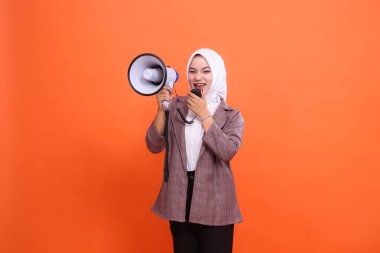 Turuncu arkaplanda izole edilmiş mikrofon hoparlörünü kullanarak bağıran tesettürlü genç Asyalı kadın, konuşma, reklam, yayın konsepti.