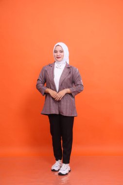 Beyaz ofis elbisesi giyen güzel Müslüman kadın modelin tam boy portresi şık tesettüre ayrılmış turuncu bir arka plan giyer. Moda, güzellik, şirket, yaşam tarzı kavramı.