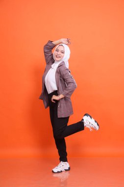 Endonezya 'nın güzel Müslüman kadın modelinin tam boy portresi neşeli dans ederken şık tesettür beyaz ofis kıyafetleri içinde izole edilmiş turuncu stüdyo arka planı giyer. Moda kavramı, güzellik, arkadaşlık
