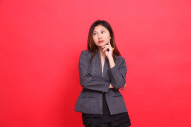 Asyalı bir ofis kadınının kollarını kavuşturarak düşünmesi, çenesini tutması, gri bir ceket ve kırmızı arka planda siyah bir etek giymesi. kurumsal kavramlar, yayınlar ve reklamlar için