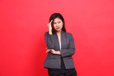 The expression of an Asian office girl with her arms in her arms is having a headache while holding it candidly wearing a gray jacket and skirt on a red background. for health and advertising clipart