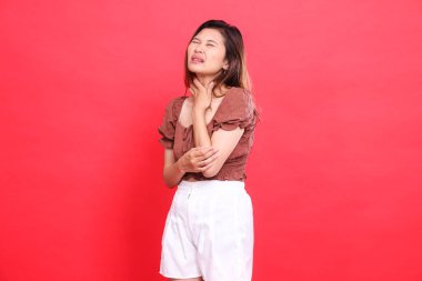 Ağır boğaz ağrısı olan Asyalı bir kızın ifadesi. İçtenlikle kahverengi bluz ve kırmızı arka planlı şort giyiyor. Sağlık, yaşam tarzı ve reklam kavramları için