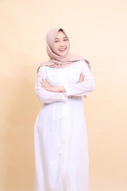 Güzel Müslüman elbisesi giyen Asyalı bir kız. Kollarını tutarken çok mutlu. Krem rengi arka planda. güzellik, model, stüdyo ve moda konsepti