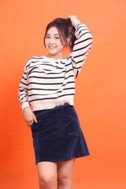 Turuncu arka planda sırtı kıllı ve plaketli neşeli Endonezyalı güzel kadın. Doğal makyaj, moda ve yaşam tarzı.