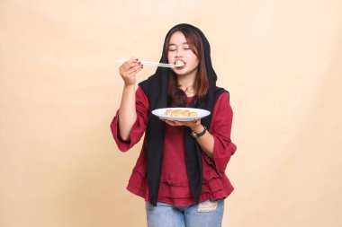 Güzel, olgun, kırmızı bir elbise giyen, tesettürlü, tesettürlü, gözlerini kapatan yemek çubuklarıyla gamzeleri ısıran ve içinde gamsum bulunan bir tabak taşıyan bir Asyalı kadın.)