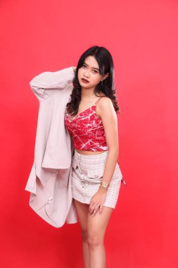 Endonezyalı zarif bir kadının portresi kırmızı desenli bir kolsuz bluz ve resmi bir krem ceket giyiyor, saçlarını elinde tutuyor. Afiş malzemesi ve reklam için izole kırmızı arkaplan.