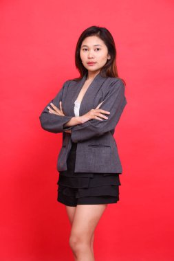 Stüdyoda gri ceket ve siyah mini etek giyen, sağ kolu çaprazlanmış, güzel, zarif bir Asyalı ofis kadınının portresi. Şirket kavramları, markalaşma ve reklamlar için