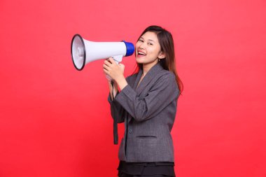 Neşeli Asyalı ofis kızı ifadesi sağa doğru eğilmiş, kameraya megafonla bağırıyor, kırmızı arka planda gri bir ceket ve etek giyiyor. Yayın ve reklam için