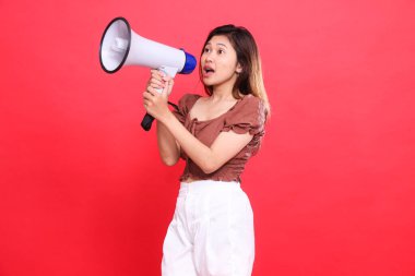 Zarif Endonezyalı kadının yüzü iki elinde ses megafonu, kahverengi bluz ve kırmızı arka planda şort tutarak bağırıyor. Yayın, teknoloji ve reklam kavramları için