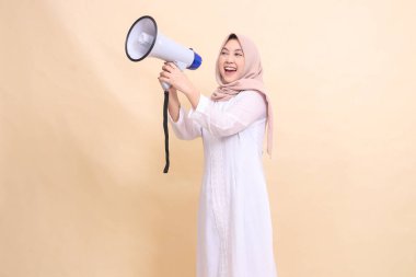 Asyalı genç kız tesettüre doğru eğilmiş iki eliyle hoparlörü tutarak neşeli bir şekilde bağırıyor. Teknoloji, yayın ve tanıtım konsepti