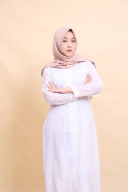 Güzel, zarif Müslüman elbisesi giyen Asyalı kadın kollarını kavuşturup krem rengi arka planda izole bir şekilde poz veriyor. güzellik, model, stüdyo ve moda konsepti