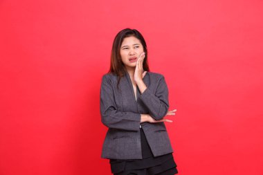 Asyalı ofis kızı ifadesi acı içinde, diş ağrısı samimi, gri ceket ve kırmızı arka planda siyah etek giyiyor. Sağlık, iş ve reklam kavramları için