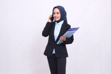 Birisi arayıp kalem, not defteri ve not defteri taşıdığında tesettürlü Asyalı seçkin bir ofis kadını ayakta duruyor. Mavi gömlekli güzel Müslüman kadın.