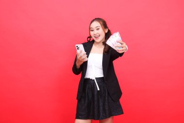 Asyalı genç, kariyer sahibi, neşeli, siyah takım elbiseli, rupiah parası ve cep telefonu taşıyan bir kadının ifadesi. Teknoloji, iş, reklam ve finansal içerik için.
