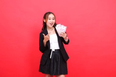 Siyah takım elbiseli neşeli Asyalı genç ofis kızı elinde rupiah para tutarken mali içerik, iş, reklam, alım satım için ona işaret ediyor.