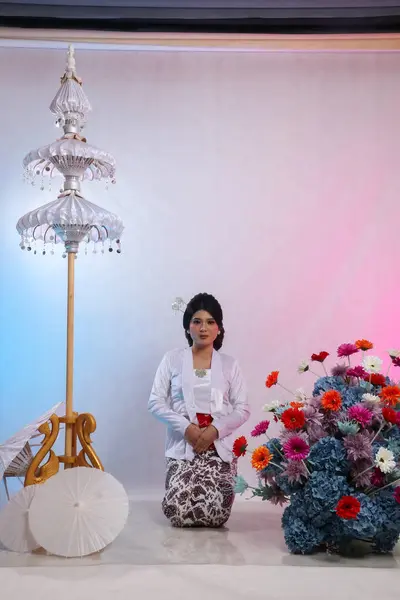 stock image full body of elegant young Asian woman squatting formally wearing modern Javanese traditional clothing, white velvet bridal kebaya on a white studio background. for advertising, beauty, fashion