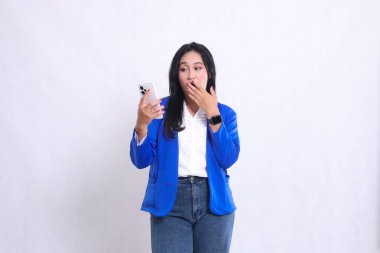 Güzel, genç bir ofis kızı mavi takım elbise giyip eli ağzını kapatırken şok edici bir şekilde akıllı telefon kullanıyor. Teknoloji içeriği, yaşam tarzı, mobil işlemler için