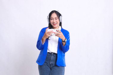 Mavi takım elbiseli güzel, yetişkin bir ofis kızı mutlu mesut çalışan bir akıllı telefon ve kulaklık kullanıyor izolasyon beyaz arka plan. teknoloji, yaşam tarzı, müzik, eğlence içeriği