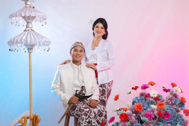 Bir çift erkek ve kadın aşığı, neşeli Asyalı genç adam, yanında keris taşıyan kadın, modern Cava geleneksel giysileri giyiyor, beyaz kadife bir kebaya gelin.