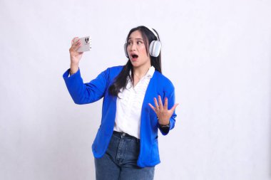 Sağ tarafta mavi takım elbiseli güzel bir ofis kadını beyaz bir arka planda izole edilmiş akıllı telefon ve kulaklıkla oyun oynarken kaybettiği için şok oldu. teknoloji, yaşam tarzı