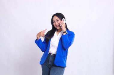 Güzel ofis kızı mavi takım elbise giyip kameraya neşeyle gülümserken akıllı telefon kullanarak izole edilmiş beyaz arka planı işaret ediyor. Teknoloji ve yaşam tarzı için.