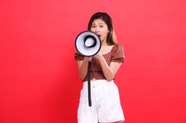 Endonezyalı bir kadın, elinde kahverengi bluz ve kırmızı arka plan olan bir ses megafonu tutarak öfkeyle bağırıyor. Yayın, teknoloji ve reklam kavramları için