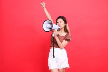 Asyalı bir kadın bağırıyor, şarkı söylüyor, samimi, elleri ses megafonunu tutuyor ve yukarı doğru sıkışıyor, kahverengi bluzunu başarıyla giyiyor, kırmızı arka plan. Yayın, teknoloji ve reklam kavramları için