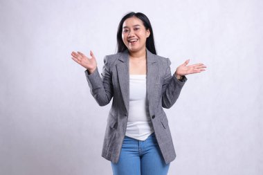 Gri ceketli ve kot pantolonlu, beyaz arka planda tek başına duran neşeli, güzel bir genç kadının iki elini de kaldırması. Reklam içeriği, moda, afiş, dergi