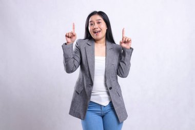 Gri takım elbiseli ve beyaz arka planda tek başına duran kot pantolonlu, neşeli genç bir kadının ifadesi. Reklam içeriği, moda, afiş, dergi