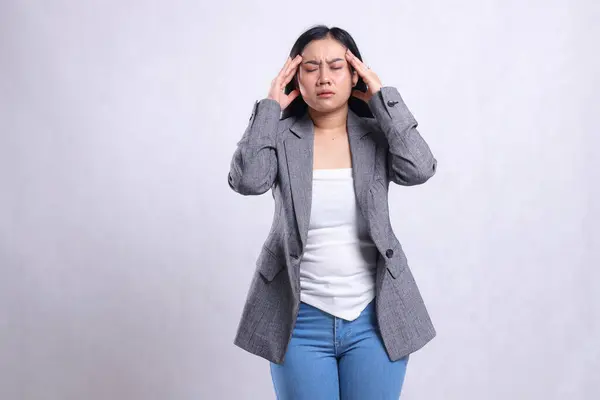 stock image expression of beautiful young office woman close eyes dizzy both hands hold head wearing gray suit and jeans standing isolated on white background. for health, medical, commercial, prevention content